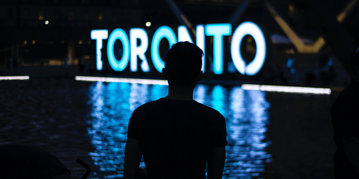 A man stands in front of the Toronto sign at Nathan Phillips Square
