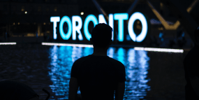 A man stands in front of the Toronto sign at Nathan Phillips Square