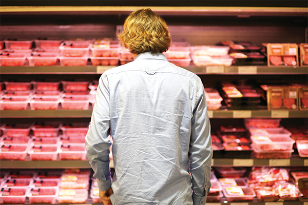 Person standing in front of the meat section at a grocery store