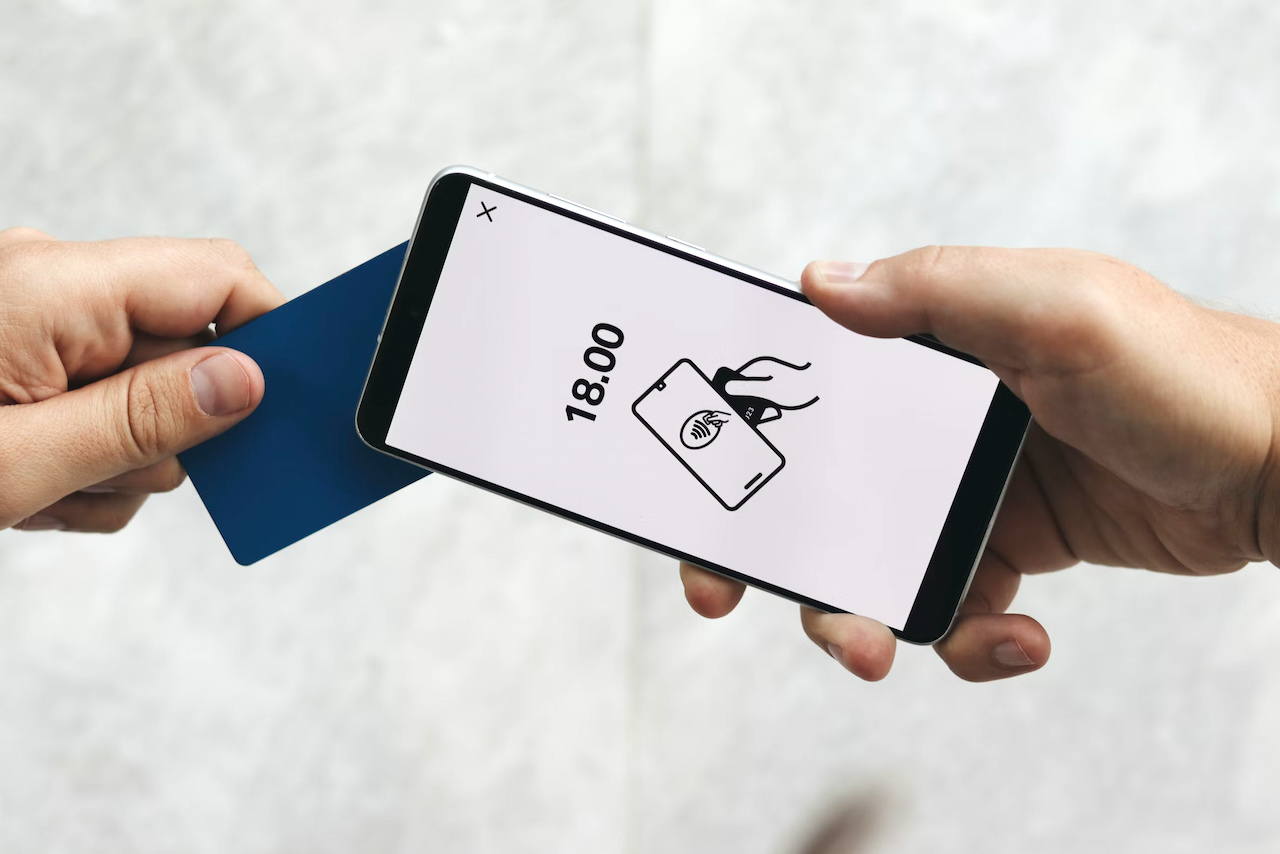 Un client tient une carte de paiement sans contact contre un iPhone affichant un écran de transaction Tap to Pay, illustrant l’acceptation des paiements mobiles sans lecteur de carte.