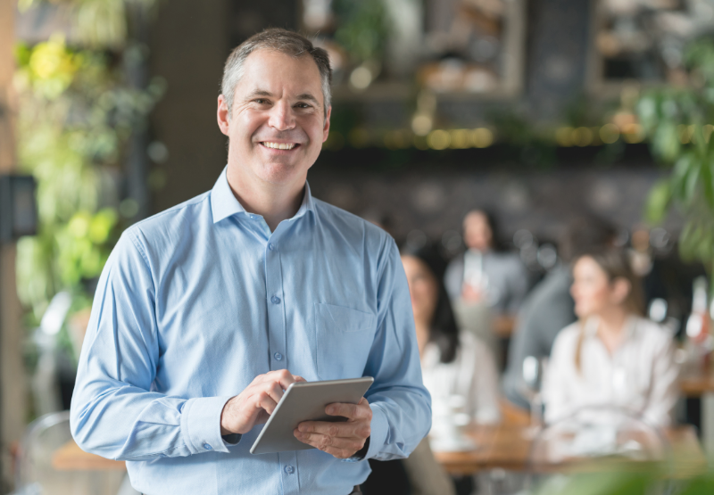 Propriétaire de petite entreprise tenant une tablette dans un établissement commercial, illustrant les possibilités de soutien et de financement pour les petites entreprises canadiennes.