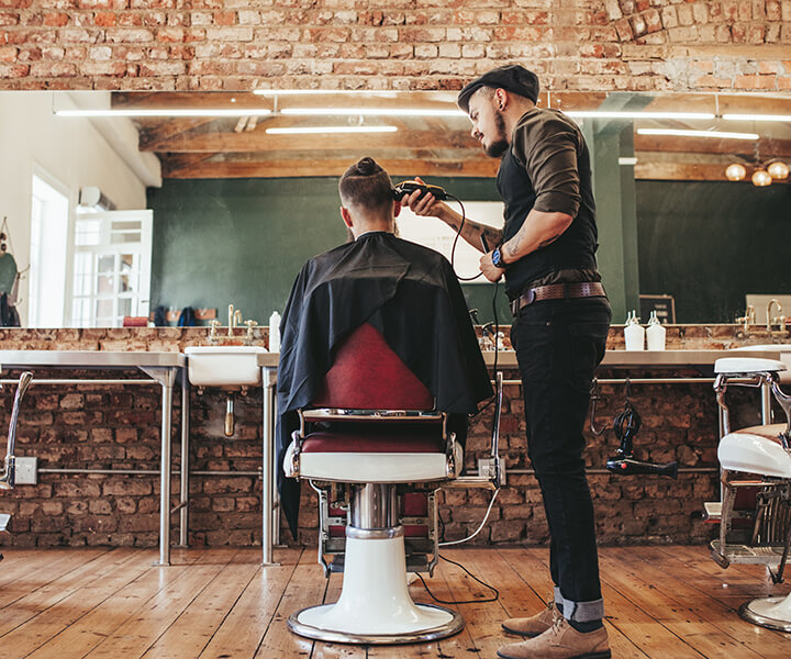 Barber giving a hair cut to person sitting in a chair in a barber shop
