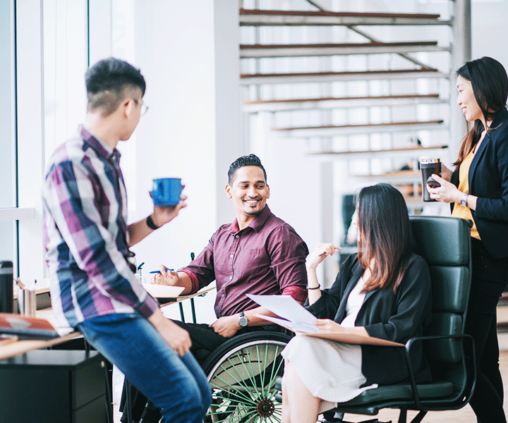 A group of employees with diverse backgrounds gather around a desk