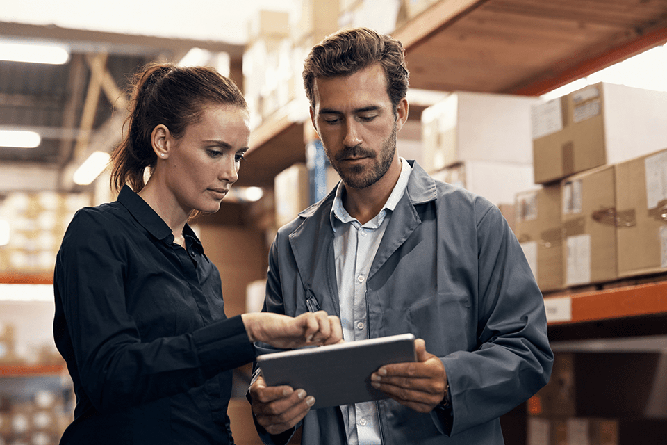 Two employees in a warehouse look at inventory management on a tablet pos solution