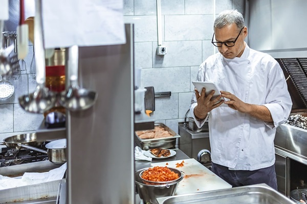 A chef in a restaurant examines an order on a tablet using the Moneris Go Appetit software