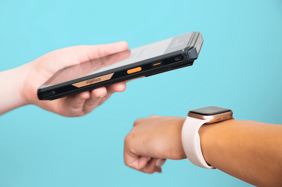 A customer pays for a purchase on their smart watch by tapping it against the Moneris Go Slim device.