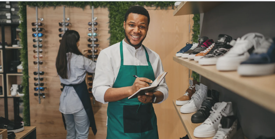 A retail associate takes inventory in a modern shoe store while another employee organizes merchandise in the background, highlighting efficient in-store operations and customer service.