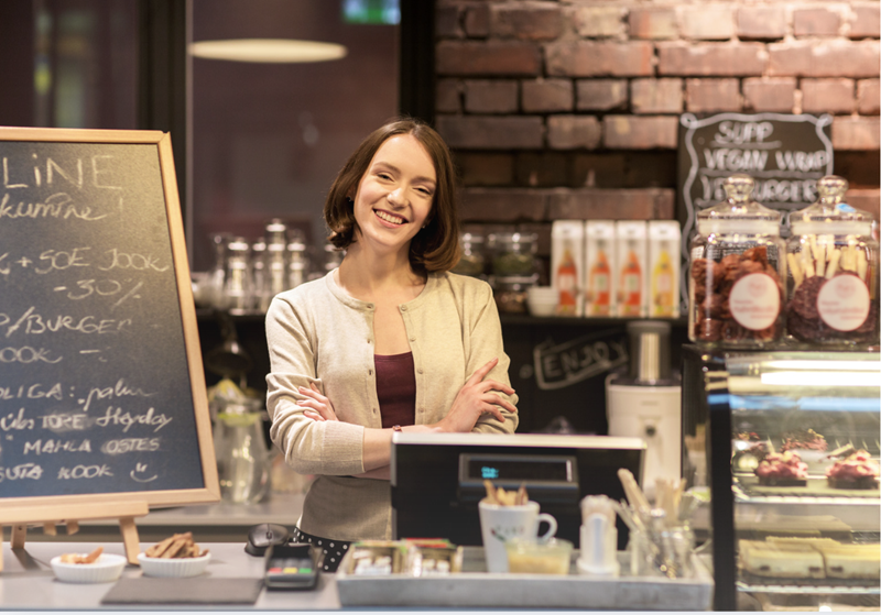 A smiling café employee standing behind the counter of a coffee shop.