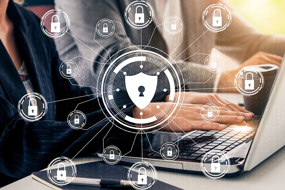 Enterprise Fraud protection concept image showing a closeup of someone using a laptop with shields superimposed overtop